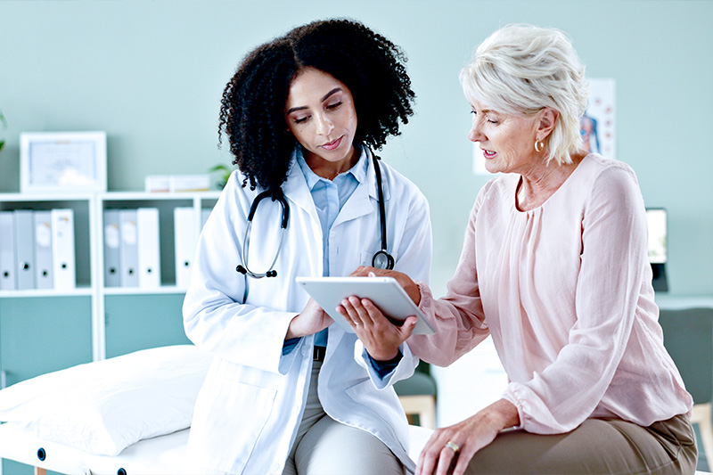 Cardiology specialist speaking with an elderly female patient, while looking at a tablet with test results.