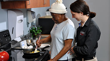 A medical worker assisting an older patient with her cooking